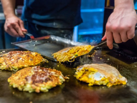 Street food vendor preparing okonomiyaki with traditional techniques.