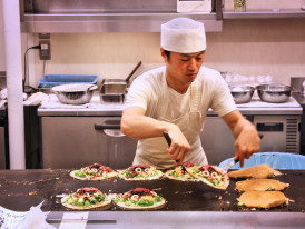 Chef preparing okonomiyaki on a large griddle 