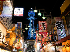 Wide view of Shinsekai’s main street with stacked signs, shops, and people walking under bright storefront lights. Image by David Dibert on Pexels.