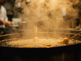 Hot oil steams as a chef prepares kushikatsu in the background of a busy Shinsekai kitchen.