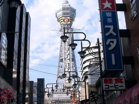 Street-level view of Tsutenkaku Tower showing its distinctive steel structure against the urban backdrop. Image by Stephen Harlan on Creative Commons Attribution 2.0