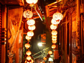 Narrow alley in Janjan Yokocho lit by hanging paper lanterns, creating a warm and nostalgic evening scene. Image by Marek Piwnicki on Unsplash.