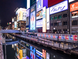 Neon signs reflecting on the canal in Dotonbori at night.