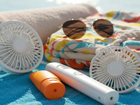 Summer essentials laid out including fan, sunscreen, and towel