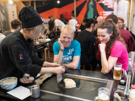 A guide showing guests how okonomiyaki is prepared at a local restaurant.