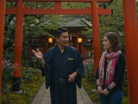 A warm exchange between host and guest at Kyoto’s famous Fushimi Inari Shrine, surrounded by vibrant torii gates.