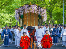 People in Heian period costumes walk in the Aoi Matsuri festival procession surrounded by Kyoto’s springtime scenery.