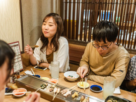 A small local izakaya with customers sitting at the counter and warm lighting