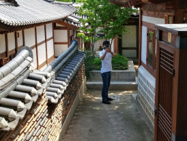 Host gesturing toward a hidden pathway between traditional buildings Photo by 주주 정 on Unsplash
