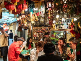 The warm, inviting exterior of a traditional izakaya with red lanterns and noren curtains in a narrow Osaka alley.