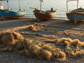 Traditional fishing boats pulled up on a pebbly beach with nets drying in the foreground
