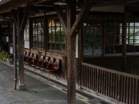 A vintage-style train station platform with wooden benches and traditional Japanese architecture surrounded by green hills Photo by Kouji Tsuru on Unsplash