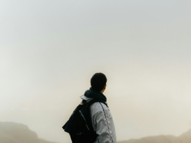 A person with a backpack standing on a mountaintop overlooking a valley filled with morning mist and distant mountains Photo by Ethan Chan on Unsplash