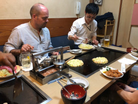 Street food vendor preparing okonomiyaki under bright lights.