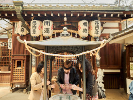 A small group of travelers discovering a tucked-away shrine hidden in a quiet Osaka alley, surrounded by stone lanterns and lush greenery. 