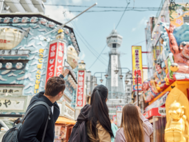 Tsutenkaku Tower rising above the bustling streets of Shinsekai district with local shops and restaurants below.