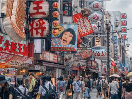 Crowded street scene in Dotonbori with people walking past illuminated food stalls.