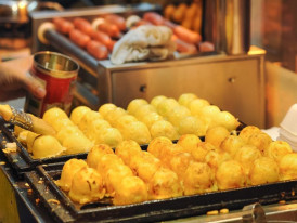Close-up of takoyaki being turned in the griddle holes, showing the cooking technique. 