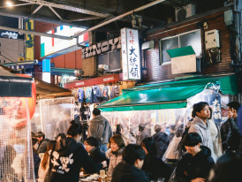 Group of locals sharing food and beer at an outdoor stall seating area Photo by Nichika Sakurai on Unsplash