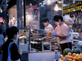 Guest and host choosing dishes at a bustling night market, pointing at various options while vendor prepares fresh food Photo by CHAN TIM on Unsplash