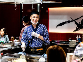 Smiling host explaining dish history to engaged guest while holding traditional cooking utensil. Photo by hiurich granja on Unsplash