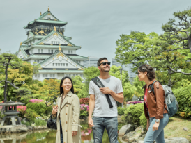Young man in casual clothes standing in front of Osaka Castle with a smile