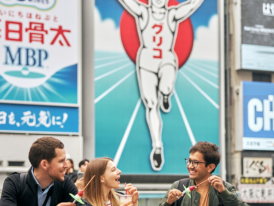 Local residents and visitors sharing street food in Dotonbori, representing cultural exchange.