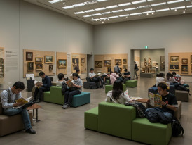 Museum visitors reading manga in comfortable indoor spaces with extensive wall collections