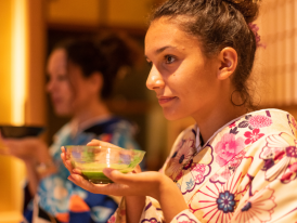 A traveler participating in a traditional tea ceremony, with a tea master demonstrating precise movements in a serene Kyoto setting