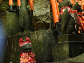 Stone fox statues with red bibs and offerings Photo by Nina Perminova on Unsplash