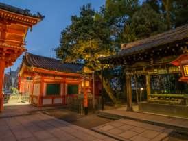 Warm lantern light illuminating stone lanterns and a vivid orange torii gate in the quiet of evening