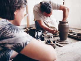 Artisan shaping clay on a spinning wheel while guiding participants in a traditional ceramics studio