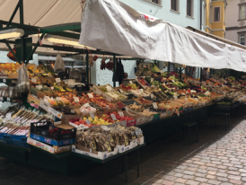 Morning produce market in a Tuscan piazza, sunlit canopy stalls and cobblestones
