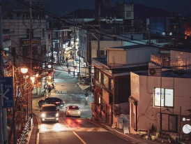 A quiet Seoul street at night with well-lit pathways and car slowly passing through the city