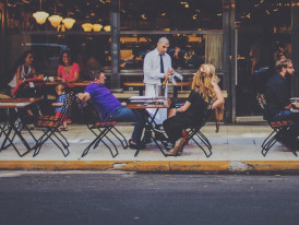 People dining at an outdoor trattoria table on a lively evening street