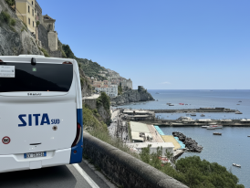 SITA bus on a cliff road and boats at the bay