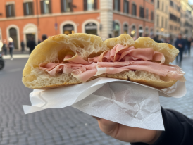 Someone holding a slice of pizza bianca with mortadella on a Roman street