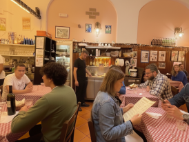 Cozy trattoria interior with locals at closely packed tables and wine bottles on shelves