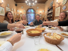 Family dinner table with hands reaching for pasta, wine glasses, and bread crumbs