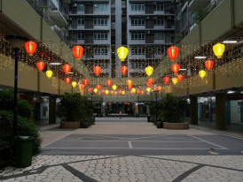 Quiet HDB void deck at night with a few people at tables under soft lighting