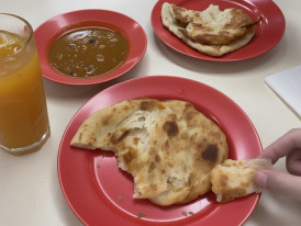 Golden roti prata torn open showing flaky layers with curry dipping sauce