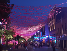 Village street at night with pink lights overhead and pedestrians