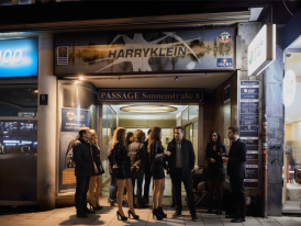 Entrance to Harry Klein club at night with line of people waiting outside