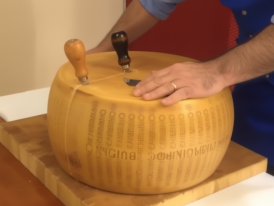 A wheel of Parmigiano Reggiano being split with knives