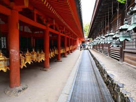 Lantern-lined walkway at Kasuga Taisha Shrine with red columns and hanging bronze lanterns
