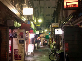 Narrow alley in Golden Gai at night with small bar entrances and illuminated signs