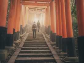 Visitors walking through vermilion torii gates at Fushimi Inari Shrine in Kyoto at dawn