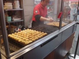 Osaka street vendor grilling takoyaki at a sidewalk food stall
