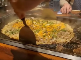 Okonomiyaki cooking on a teppan grill in Tokyo, with cabbage, egg, and savory batter being prepared fresh