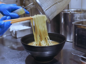 Fresh ramen noodles being lifted into a steaming bowl of broth in a Tokyo ramen kitchen